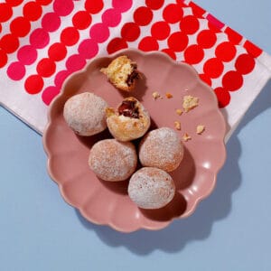 A plate, viewed from above, containing six of our delicious Mini Chocolate Hazelnut Beignets. Two of the beignets have been opened and the filling can be seen inside.