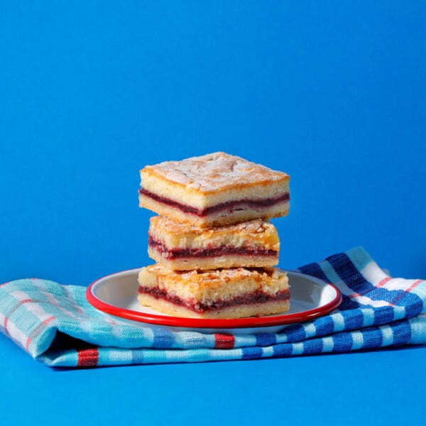 Stack of Bakewell Slice squares on a plate with checkered napkin - buttery layers and cherry jam visible.