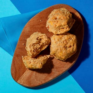 Overhead view of three vegan Cheeze and Facon scones on a chopping board with a blue napkin on a contrasting blue background.