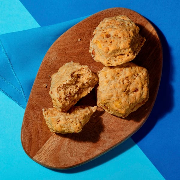 Overhead view of three vegan Cheeze and Facon scones on a chopping board with a blue napkin on a contrasting blue background.