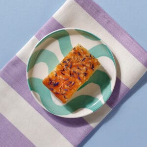 Close-up of Lemon Drizzle Cake slice topped with sugar and edible flower petals.