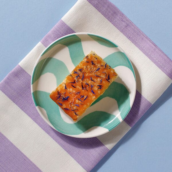 Close-up of Lemon Drizzle Cake slice topped with sugar and edible flower petals.