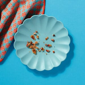 Empty blue plate with crumbs from Maple and Pecan Flapjack on orange patterned napkin.