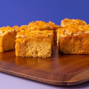 Close up of Orange Almond and Polenta Traycake squares topped with almonds and orange slices.