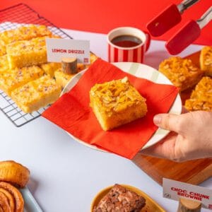 Hand serving a slice of Orange Almond and Polenta Traycake onto a plate.