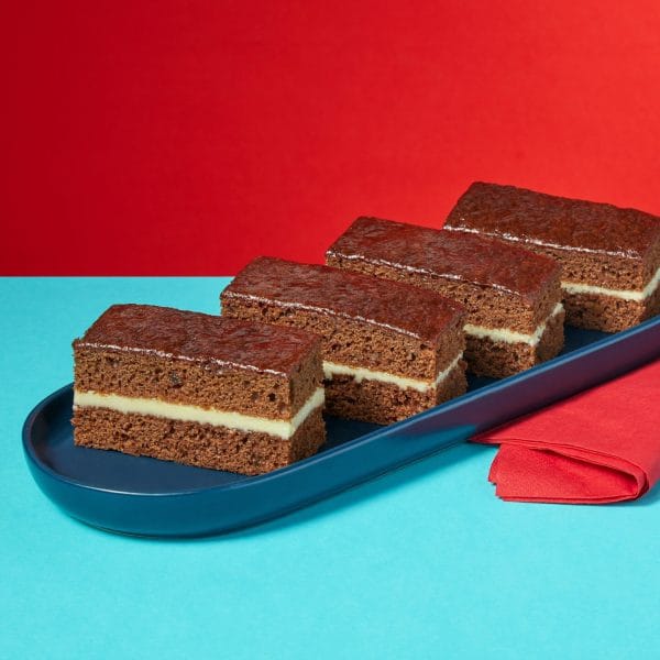 Rum and Ginger Traycake slices on a dark blue plate against a red background.