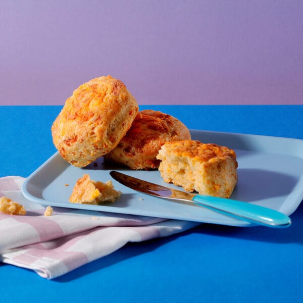The Big Cheese scones stacked on blue plate showing golden tops and melted cheese crust.