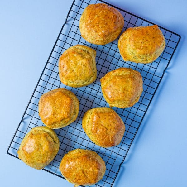 Overhead view of eight Spinach and Feta Scones on a cooling rack over a blue background.