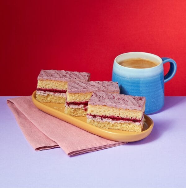 Blackberry and Mascarpone Traycake slices stacked beside a blue coffee mug on a red background.