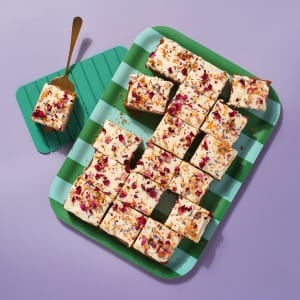 A whole tray of carrot cake on a green striped tray on a purple background.