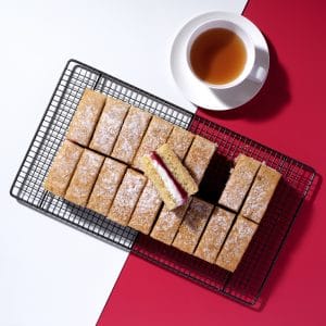 Pre-cut Victoria Sponge Traycake on cooling rack with cup of tea, Cake Club.