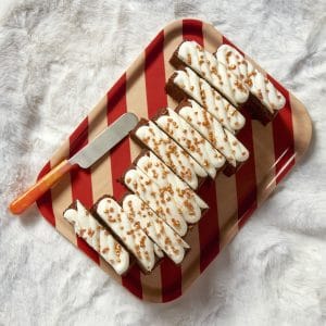 A rum and raisin Christmas loaf cake on a red striped tray with a drizzle of icing and a spreading knife beside it.