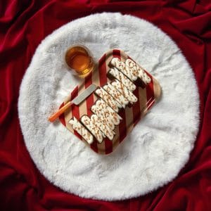 A rum and raisin Christmas loaf cake topped with icing and caramel drizzle, styled with a wooden spoon on a white faux fur mat.