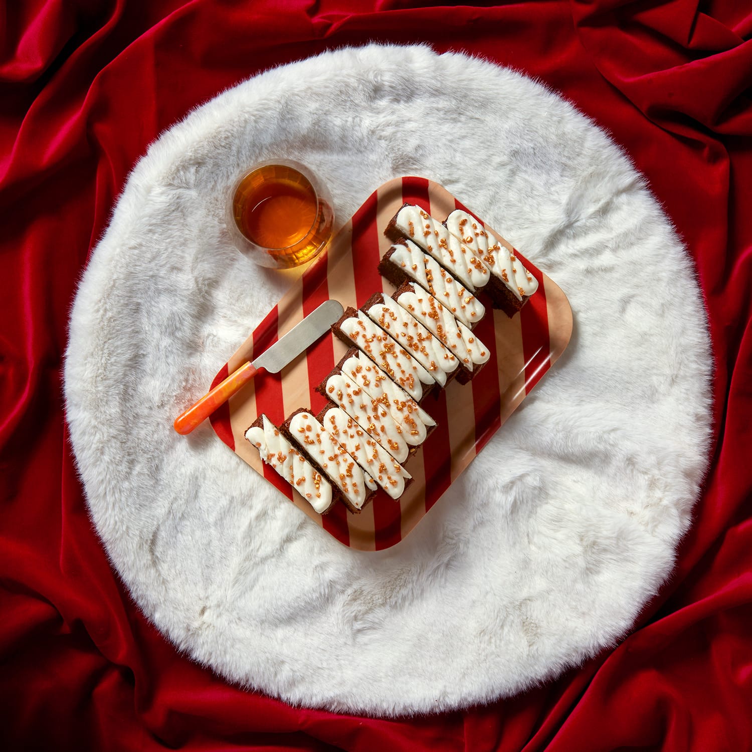 A rum and raisin Christmas loaf cake topped with icing and caramel drizzle, styled with a wooden spoon on a white faux fur mat.