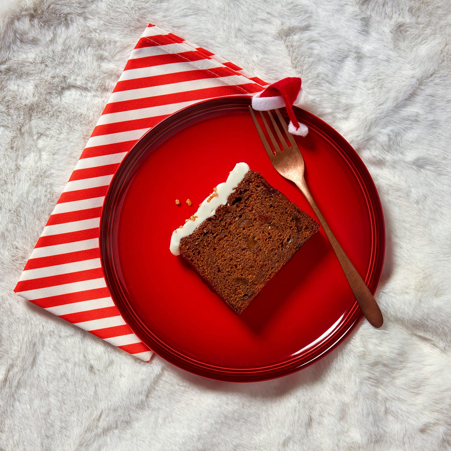 A single slice of rum and raisin Christmas loaf cake on a red plate with a striped napkin and spoon.