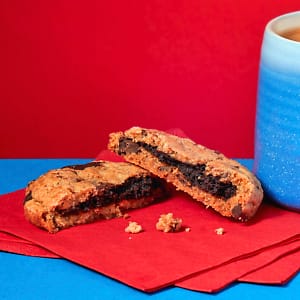 Zoomed in view of a Loaded Chocolate Chip Cookie broken open on a blue plate against a red background.