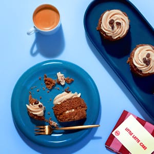 Overhead view of the Little Latte Mini Cake, a small coffee flavoured cupcake with crumbs scattered around it on a blue plate.