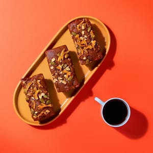 Vegan Sticky Ginger and Lemon Mini Loaf topped with lemon zest and seeds beside white mug for café display.